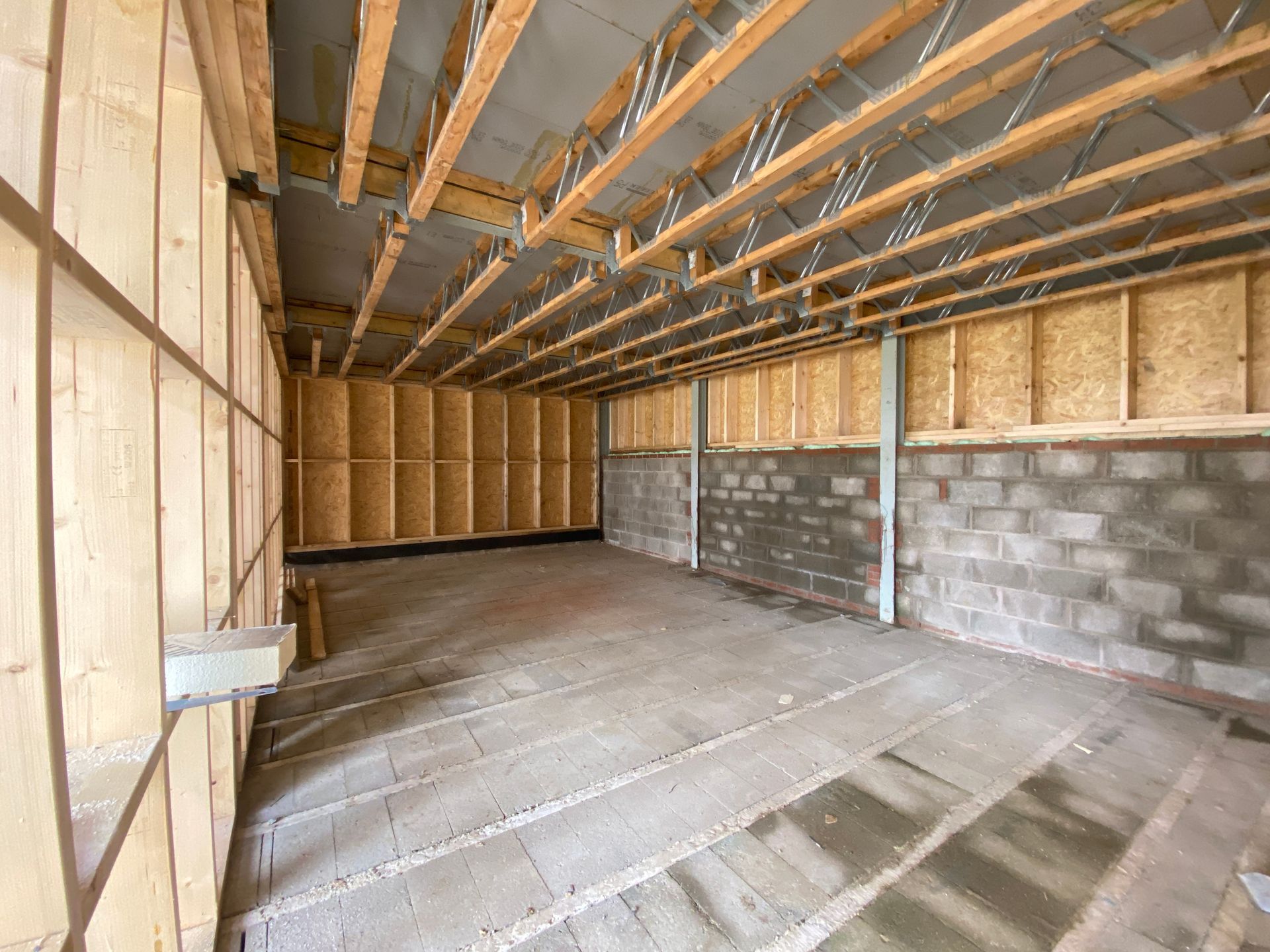 Interior view of a building under construction, showing wooden beams, walls, and a concrete floor.