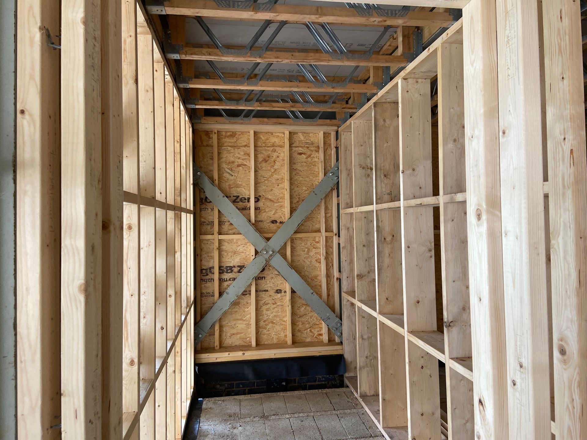 Interior view of a narrow, wooden-framed hallway under construction; includes bracing and OSB sheathing.