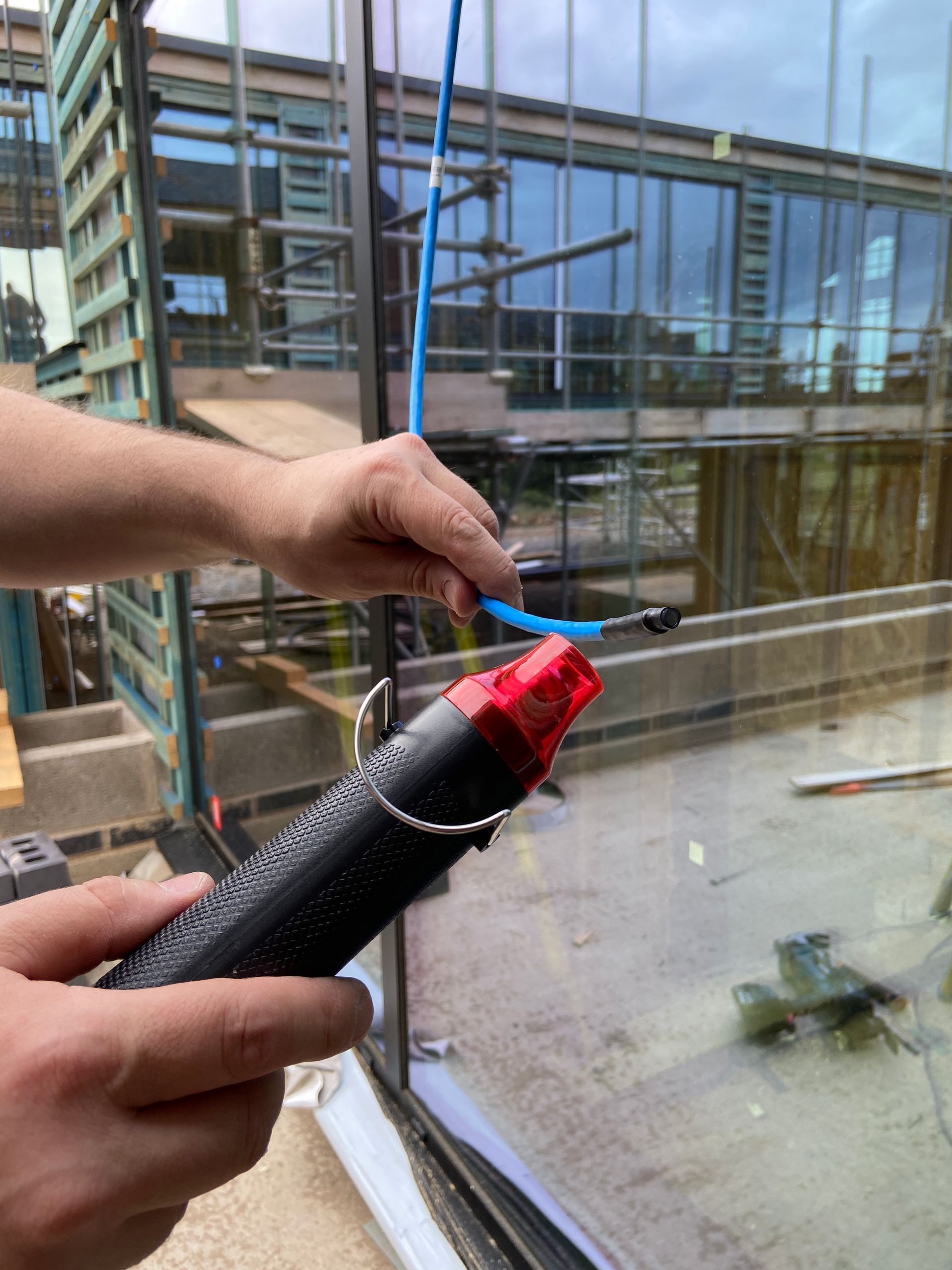 Person using a heat gun on a blue cable near a glass building under construction.