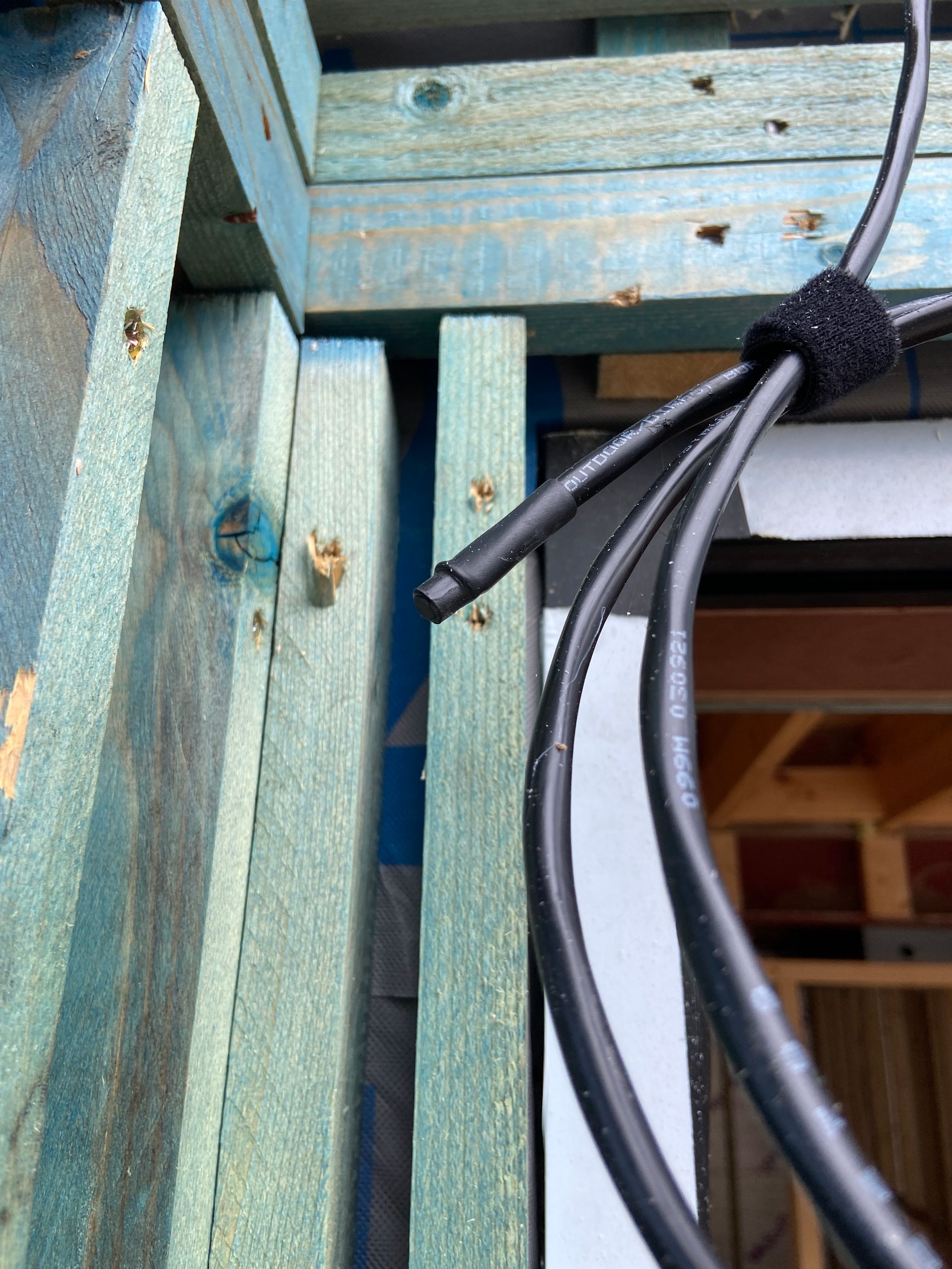 Close-up of black cables secured to blue wooden framing with a velcro strap.