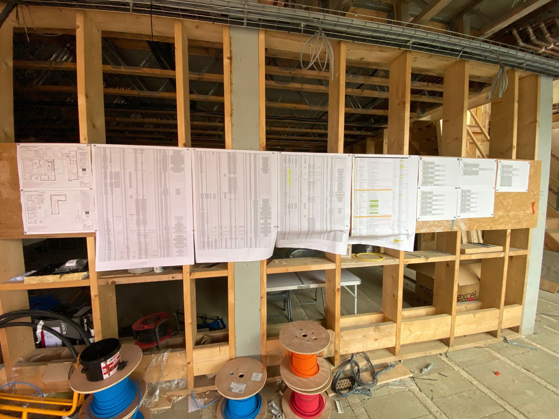 Interior wall under construction with wooden framing, electrical plans, and spools of wire.