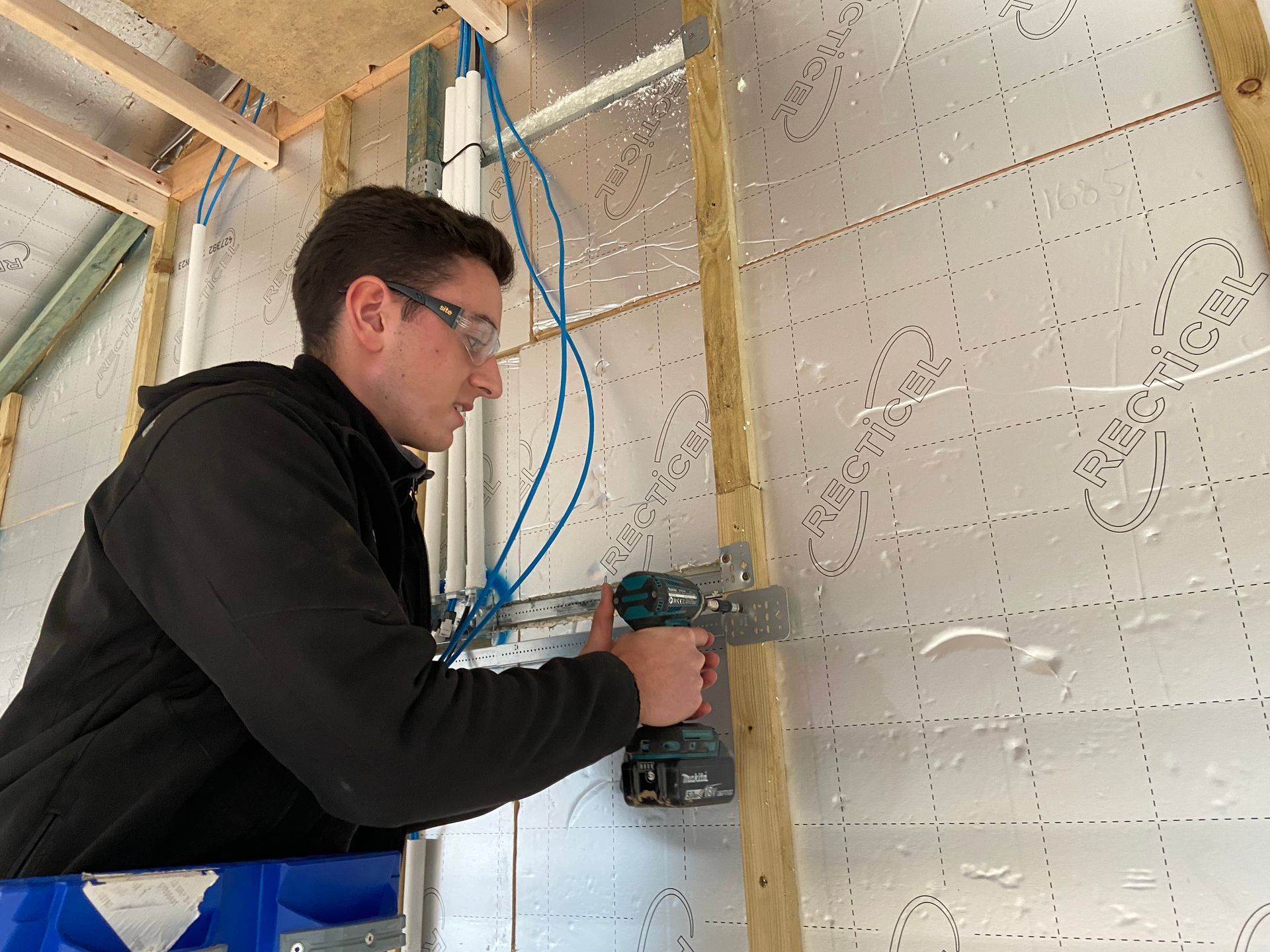 Photo of someone using a driver to attached a back box strap to provide support for metal back boxes