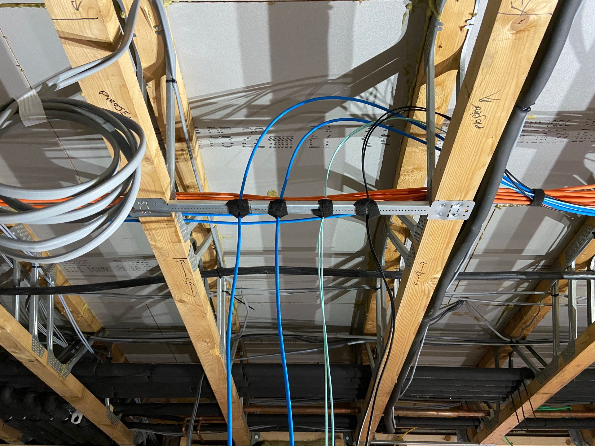 Electrical wiring and conduit secured to exposed wooden ceiling beams.