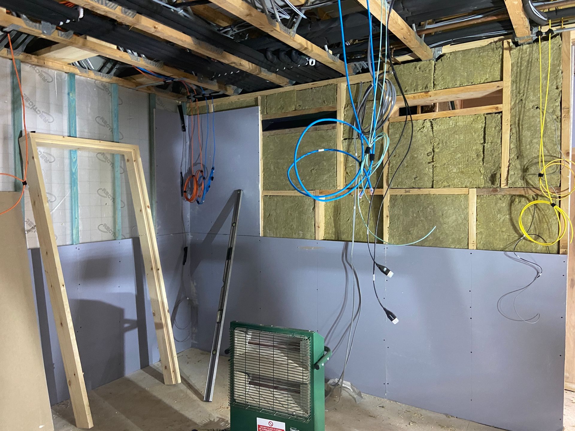 Interior construction: insulation, wiring, gray wall, wooden frame, green heater.