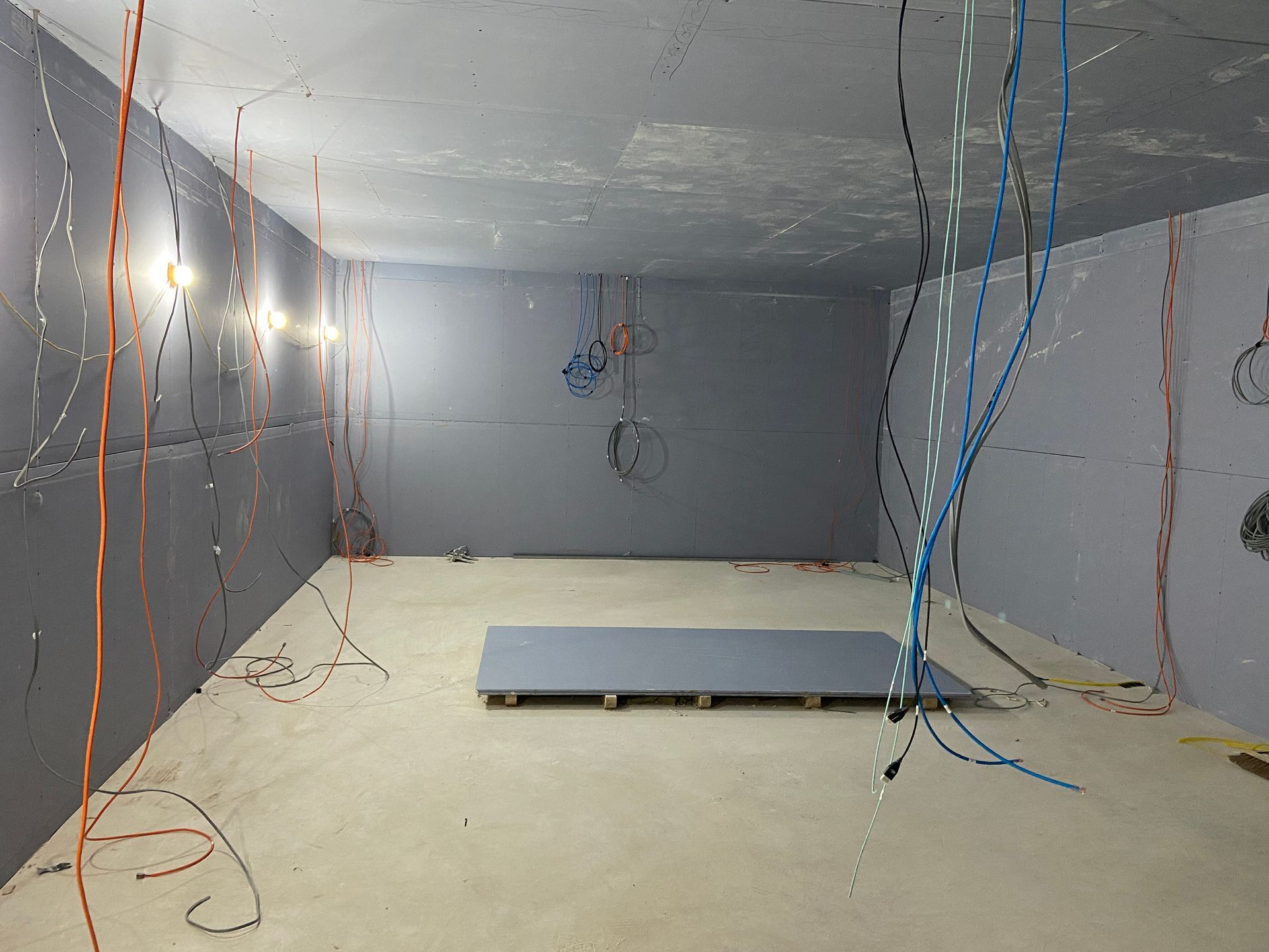 Interior of a gray-walled room with exposed wires hanging from the ceiling and walls; a raised platform sits on the floor.
