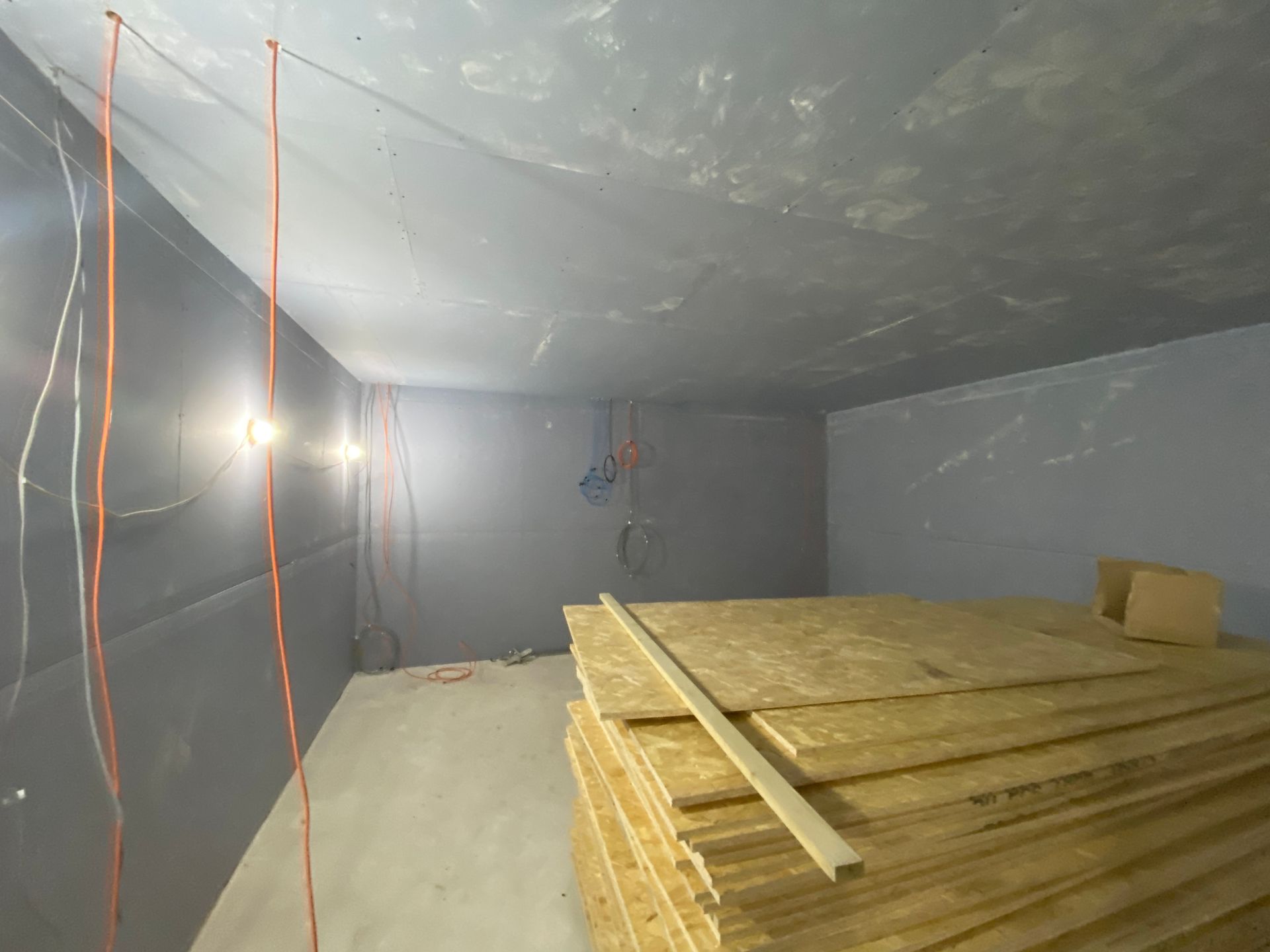 Interior of a room under construction with exposed wiring, gray walls, and stacked wood panels.