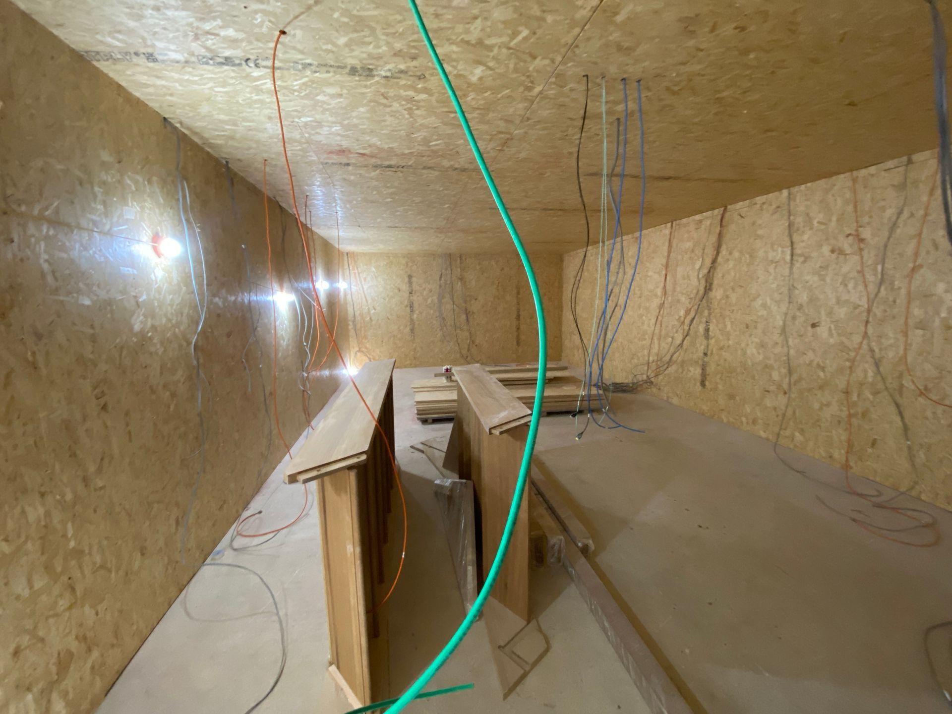 Inside a wood-paneled room, construction in progress. Green wire arches; various wires hang from ceiling.