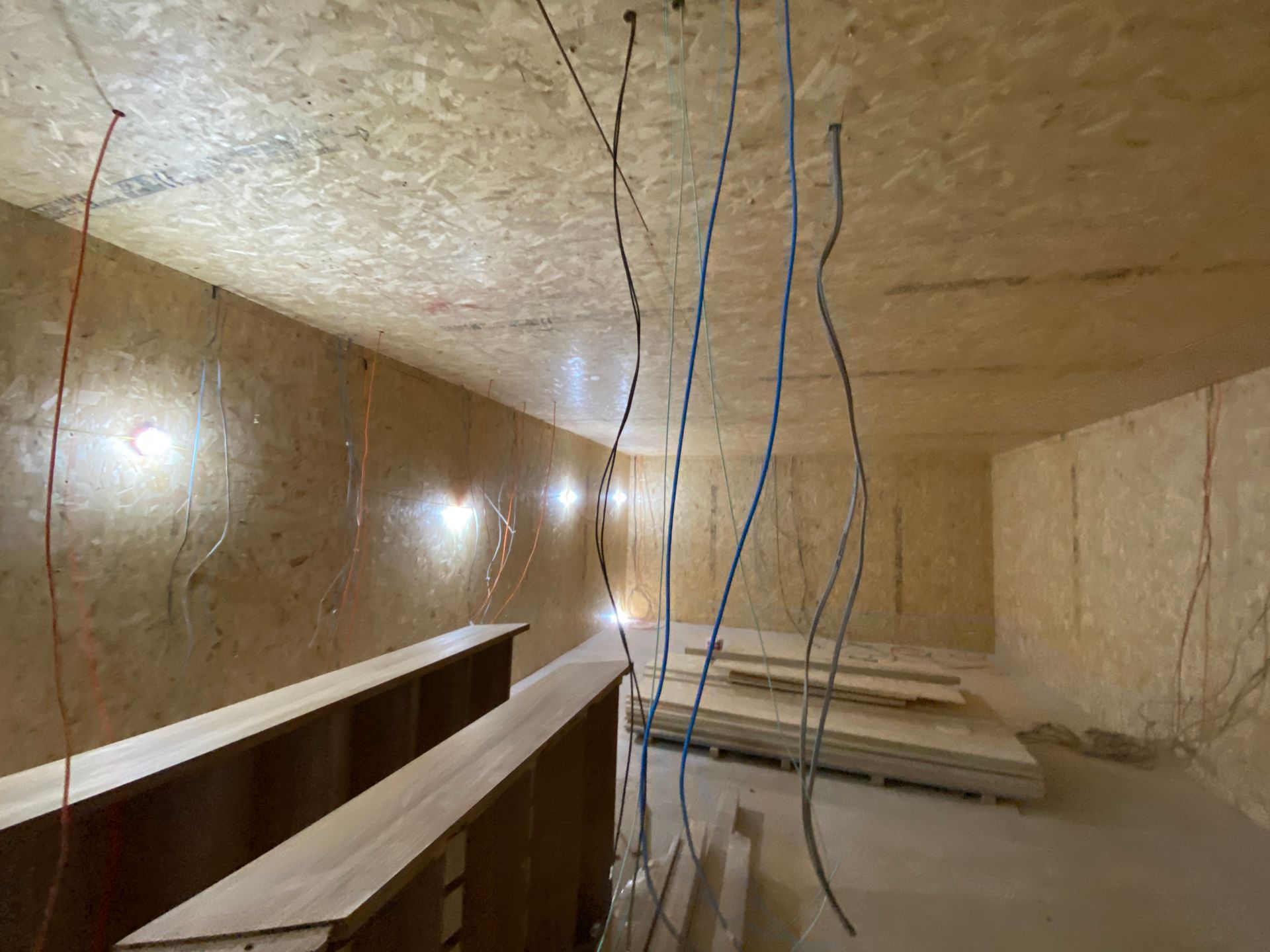 Interior construction: OSB-paneled room with hanging wires, potential lighting, and stacked wood.