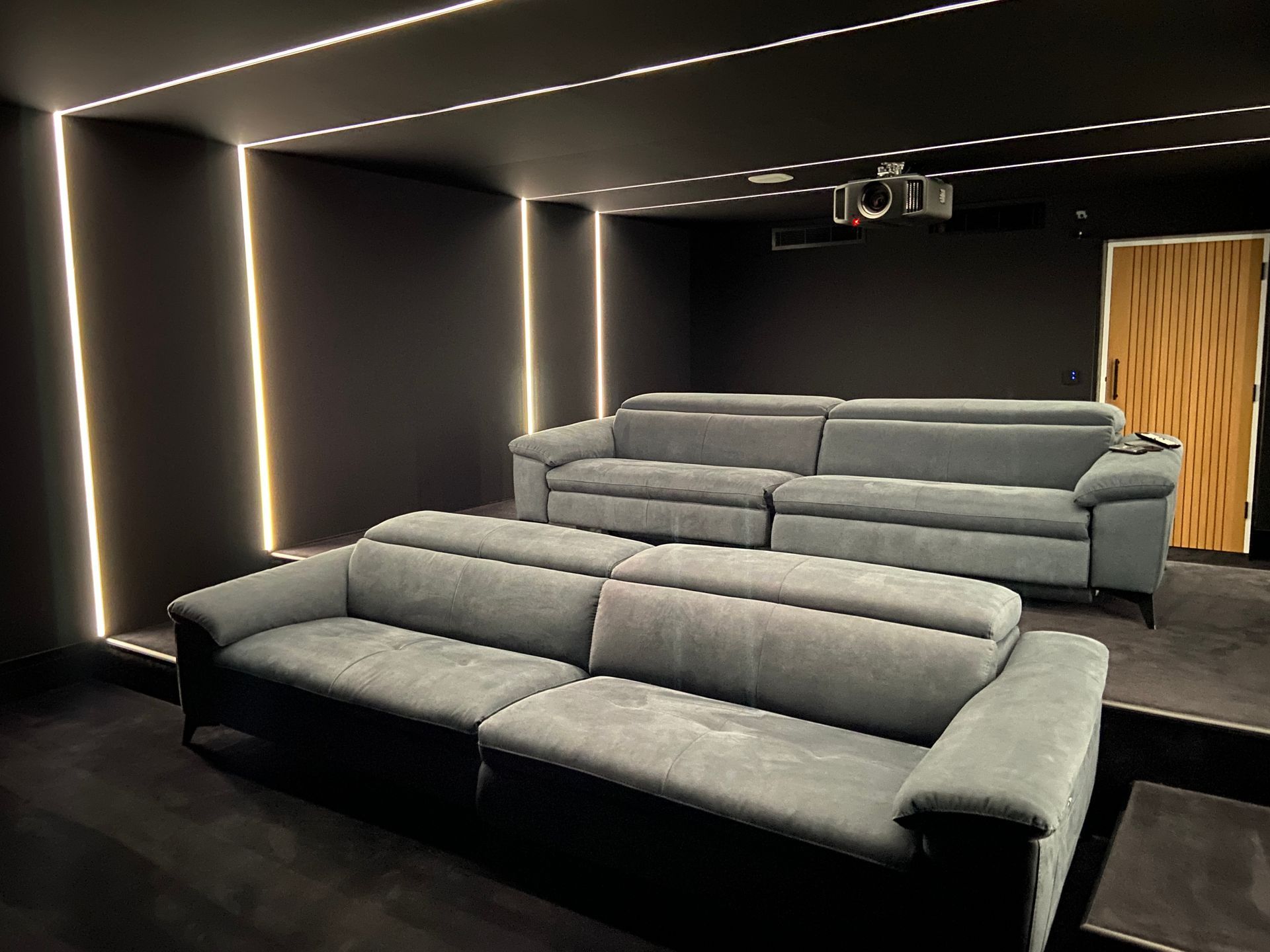 Dark home theater with gray sofas, a projector, and recessed lighting.