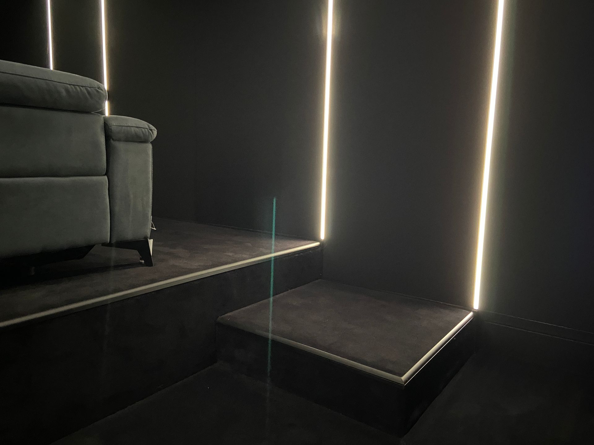 Dark room with lit lines on wall, a gray couch on a raised platform, and a step.