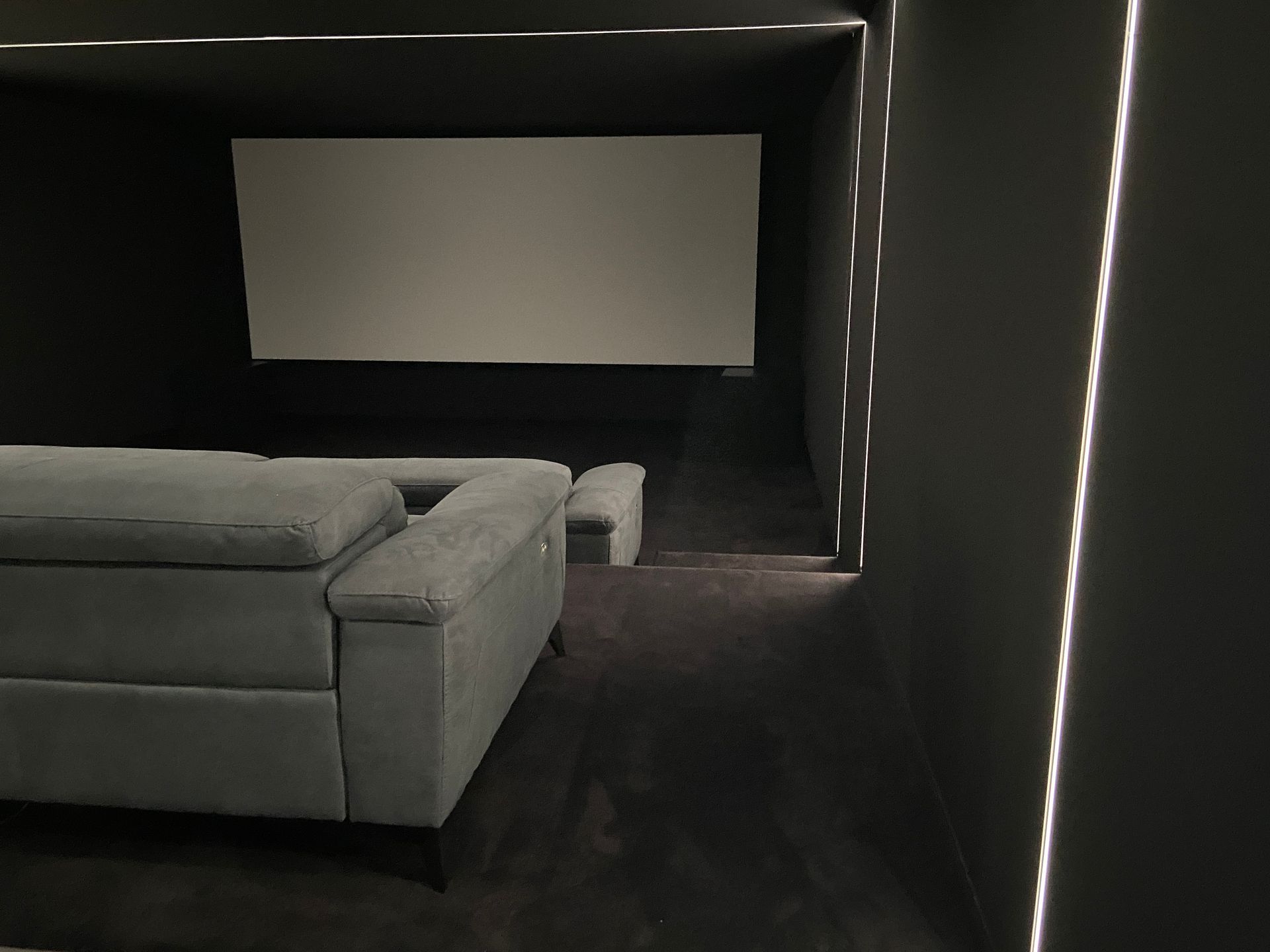 Dark home theater with a gray couch facing a white screen. LED lights line the walls.