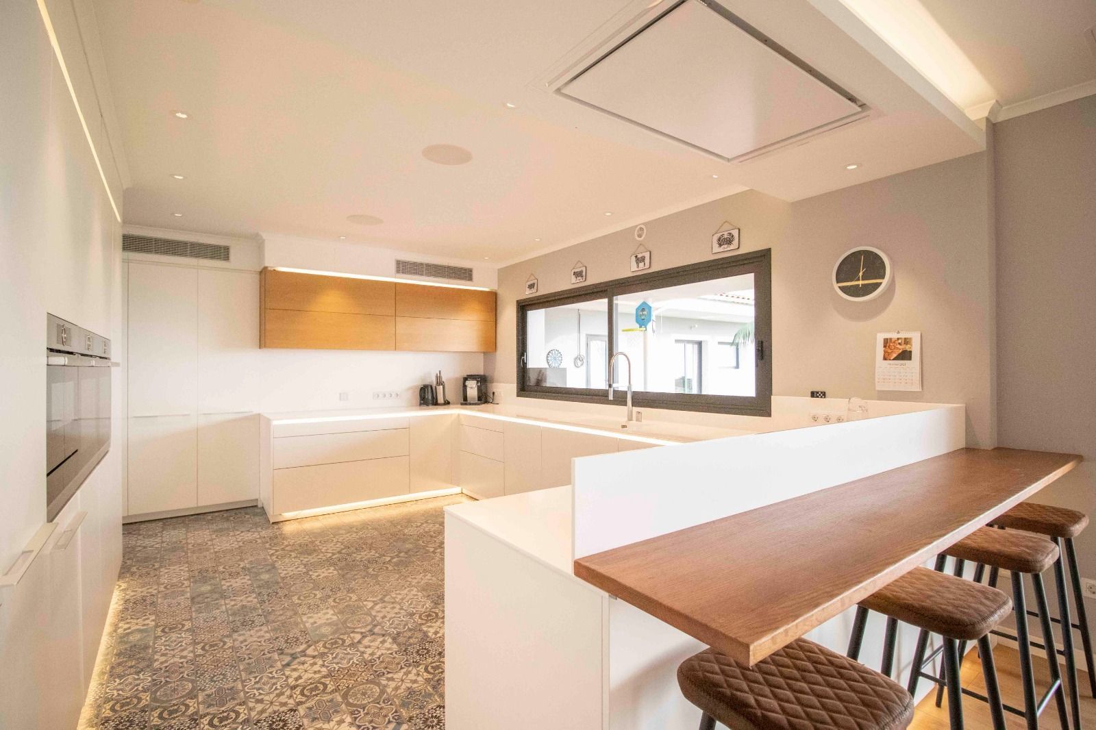 Modern kitchen with white cabinetry, wooden countertop and stools, gray floor, and large window.