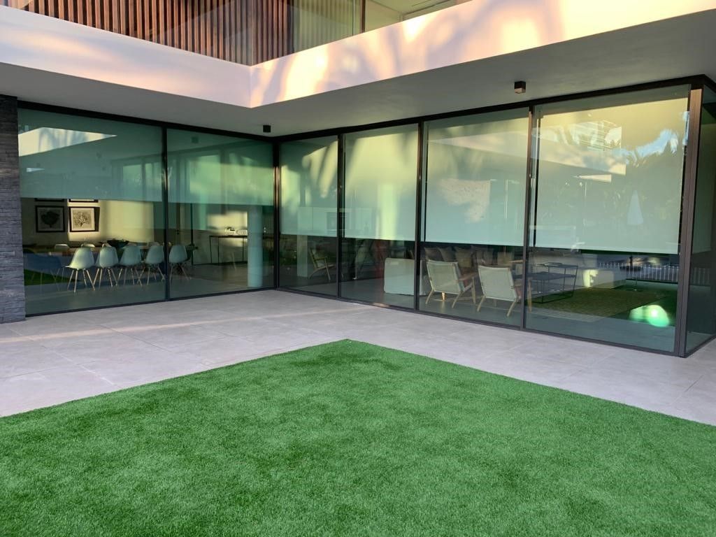 Modern home with green grass, glass walls, and partially drawn blinds.