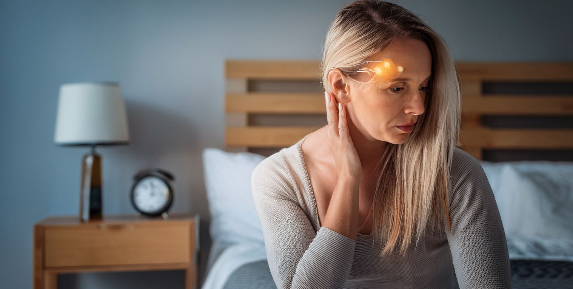 Woman in bedroom, holding neck, appears to have a headache. Lit up area on head.