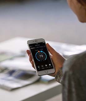 A photograph of someones hand holding a mobile phone using the Control4 mobile application to adjust heating