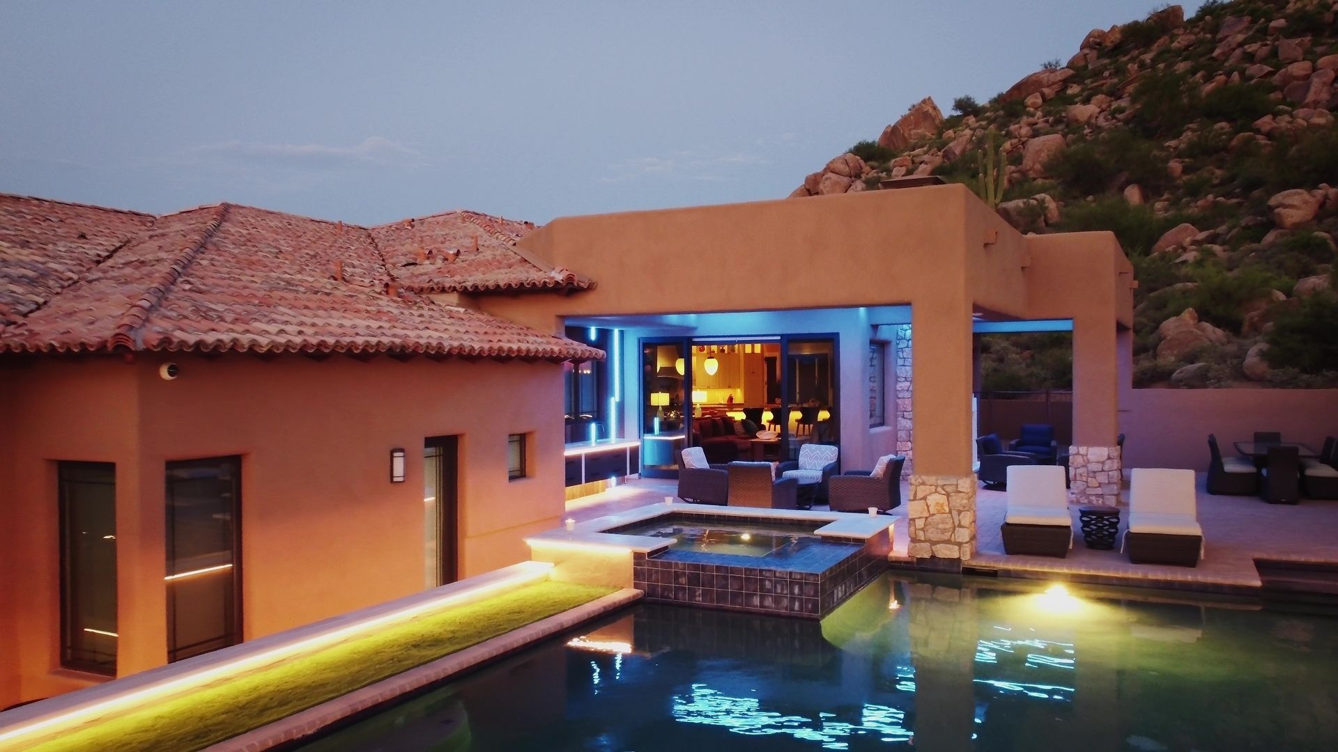 Luxury home with pool lit at dusk; southwest style, rocky background.