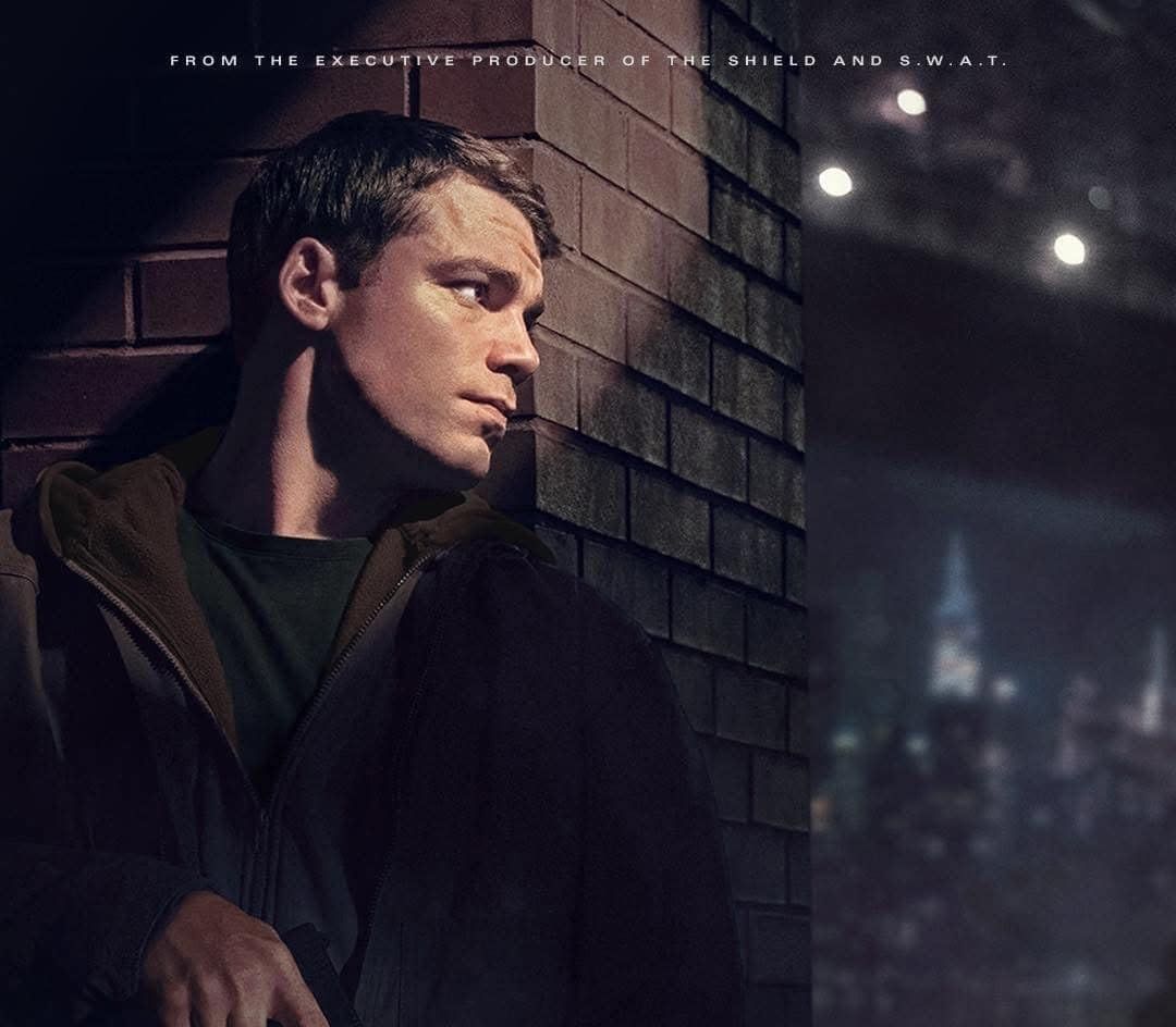 A poster for the tv series The Night Agent showing A spy leaning against a brick wall with a city in the background.