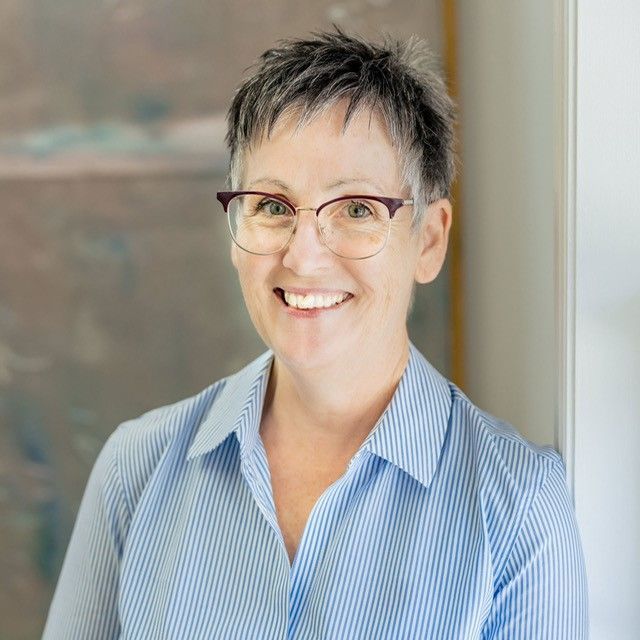 A woman wearing glasses and a blue shirt is smiling for the camera.