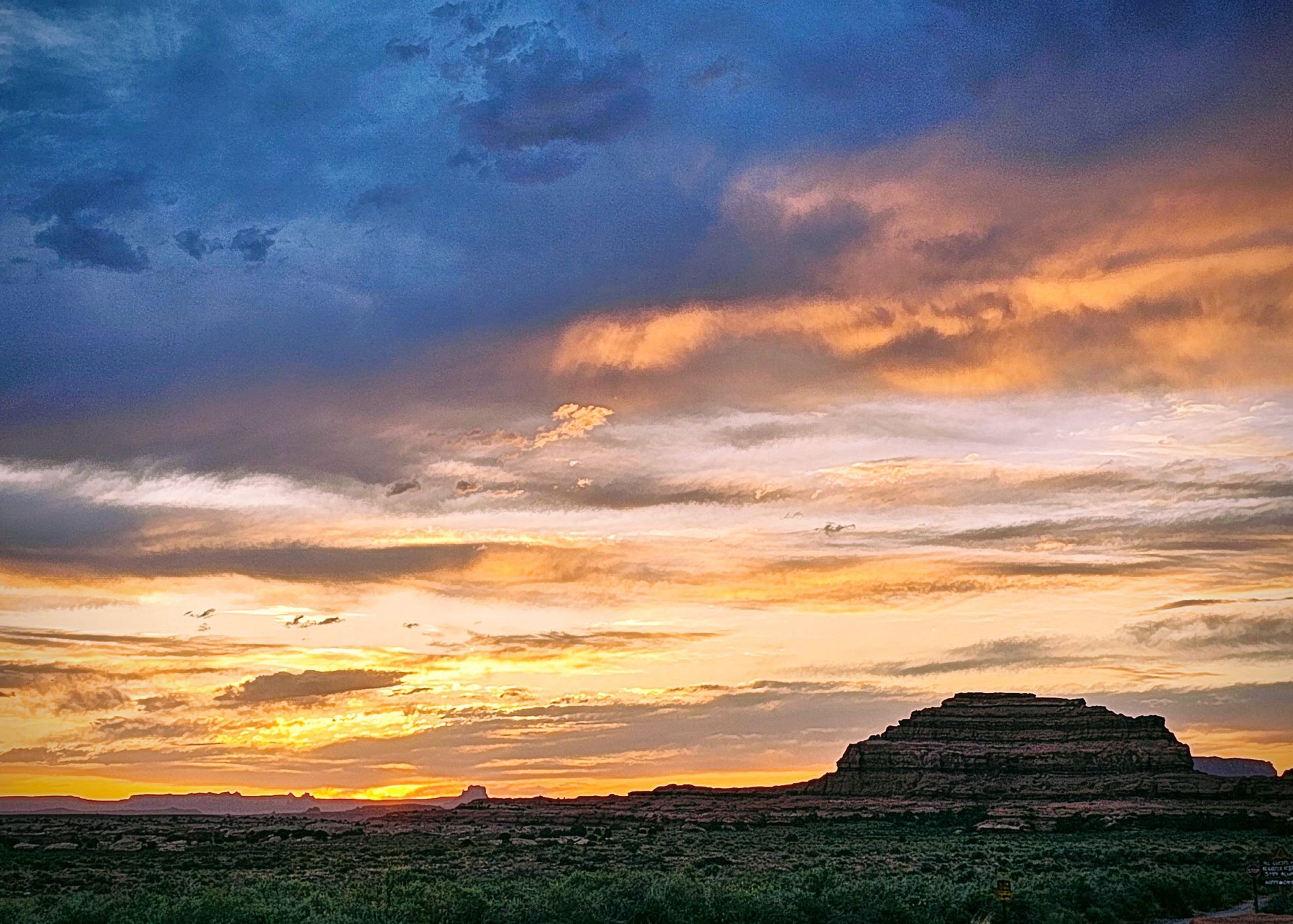 A sunset over a desert with a large rock in the foreground.