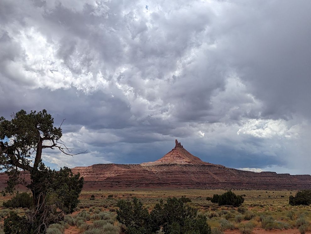 A desert landscape with a mountain in the background and clouds in the sky