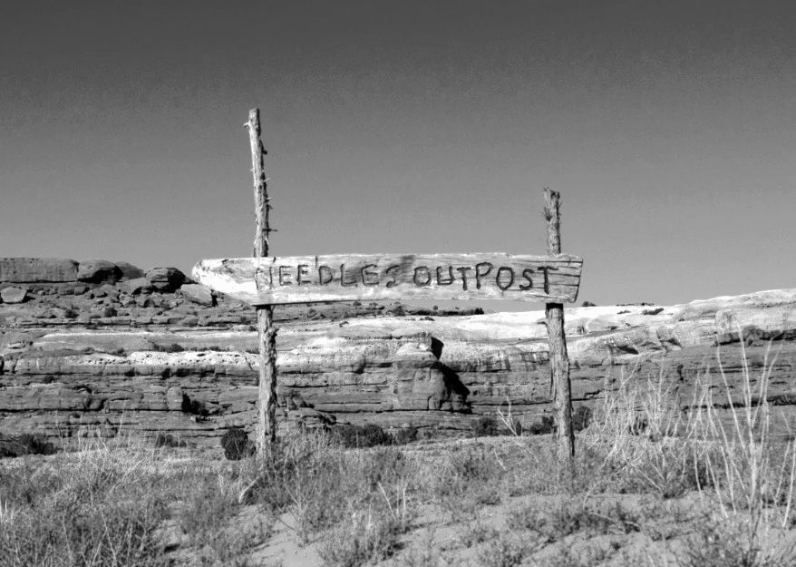 A black and white photo of a wooden sign that says need a outpost