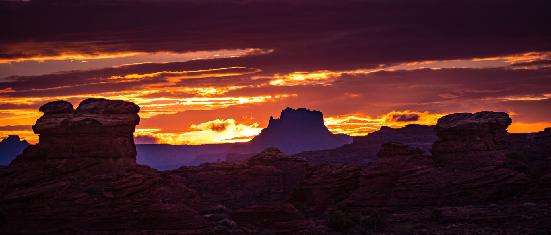 A sunset over a desert landscape with rocks in the foreground.