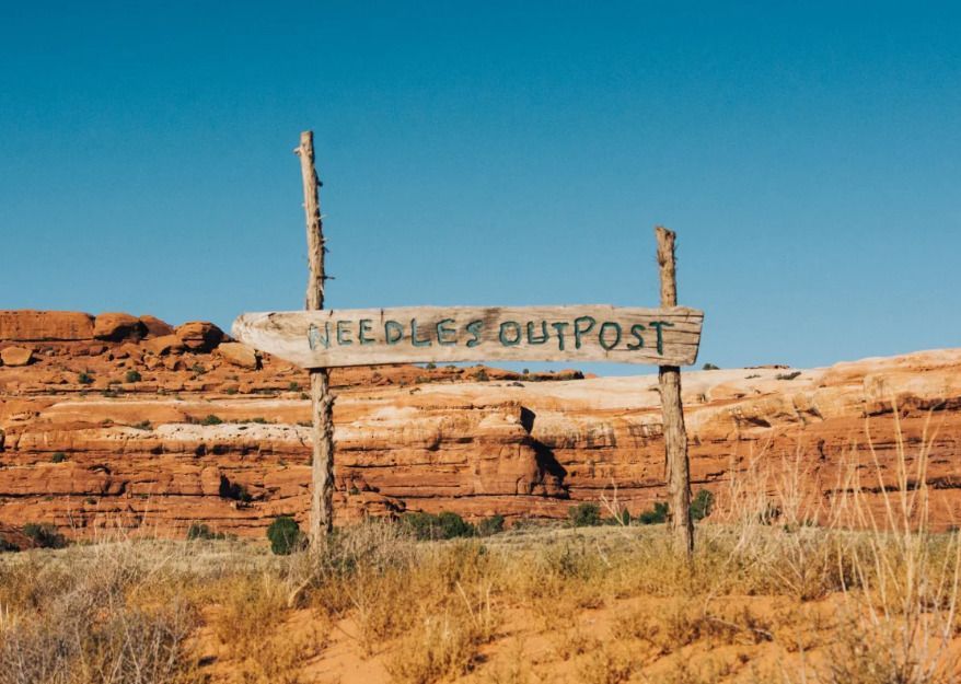A wooden sign in the middle of a desert says `` needless outpost ''.