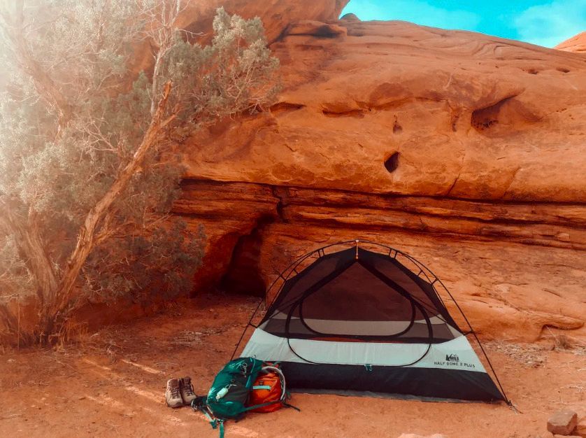 A tent is sitting under a rock in the desert.