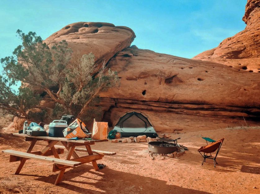A picnic table and chairs are sitting in front of a tent in the desert.
