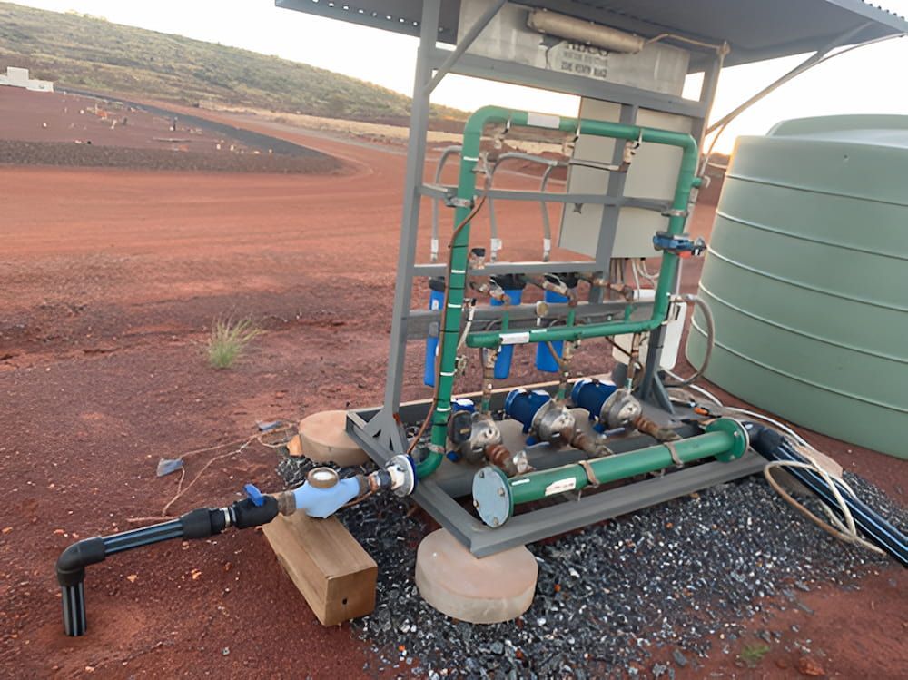 A Water Pump Is Sitting In The Dirt Next To A Green Tank — DAVMAC Plumbing in Wauchope, NSW