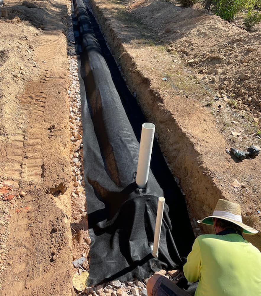 A Man In A Hat Is Sitting In A Trench Next To A Pipe — DAVMAC Plumbing in Wauchope, NSW