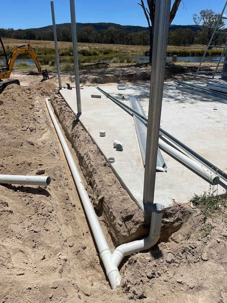 A Construction Site With Pipes In The Dirt And A Yellow Excavator — DAVMAC Plumbing in Wauchope, NSW
