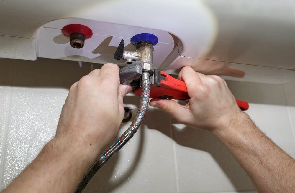 A Person Is Fixing A Water Heater With A Wrench — DAVMAC Plumbing in Laurieton, NSW