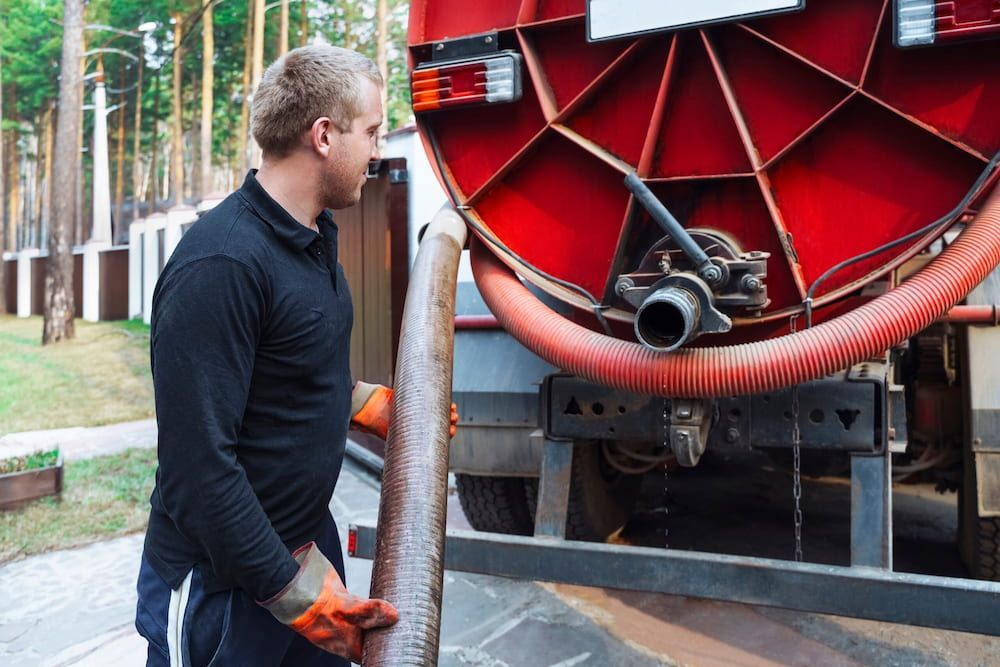 A Man Is Standing In Front Of A Vacuum Truck Holding A Hose — DAVMAC Plumbing in Wauchope, NSW