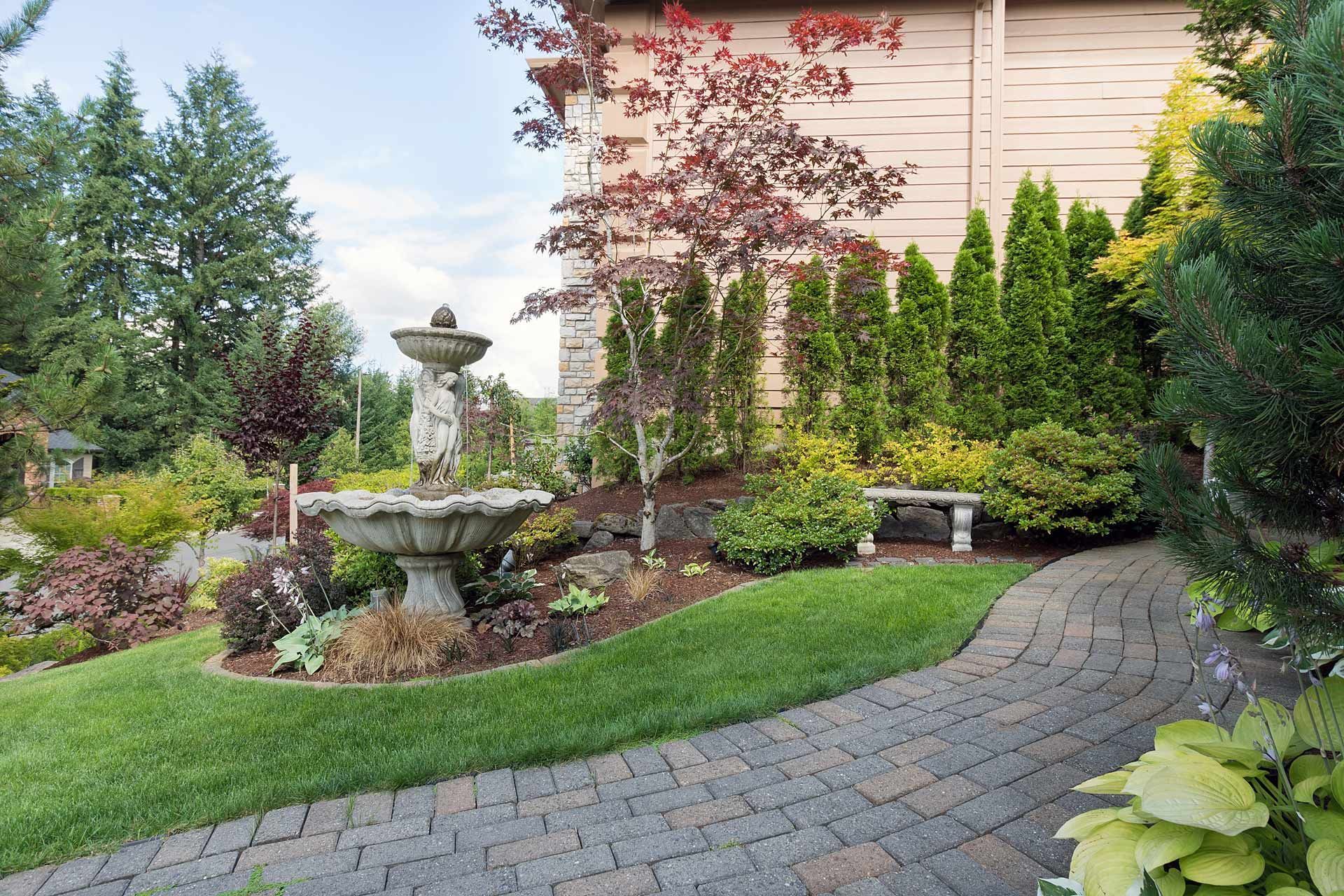 Stone fountain in a landscaped garden, with a brick pathway and manicured lawn.