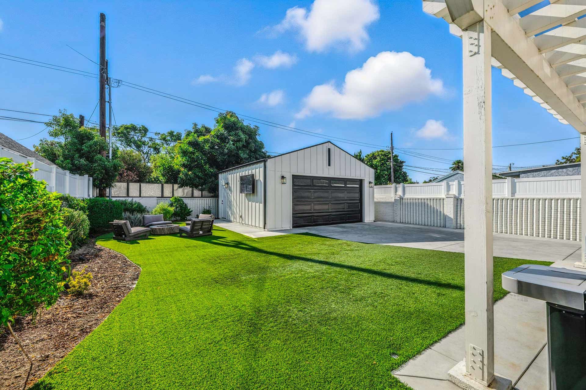 Backyard with green grass, white garage, and blue sky.