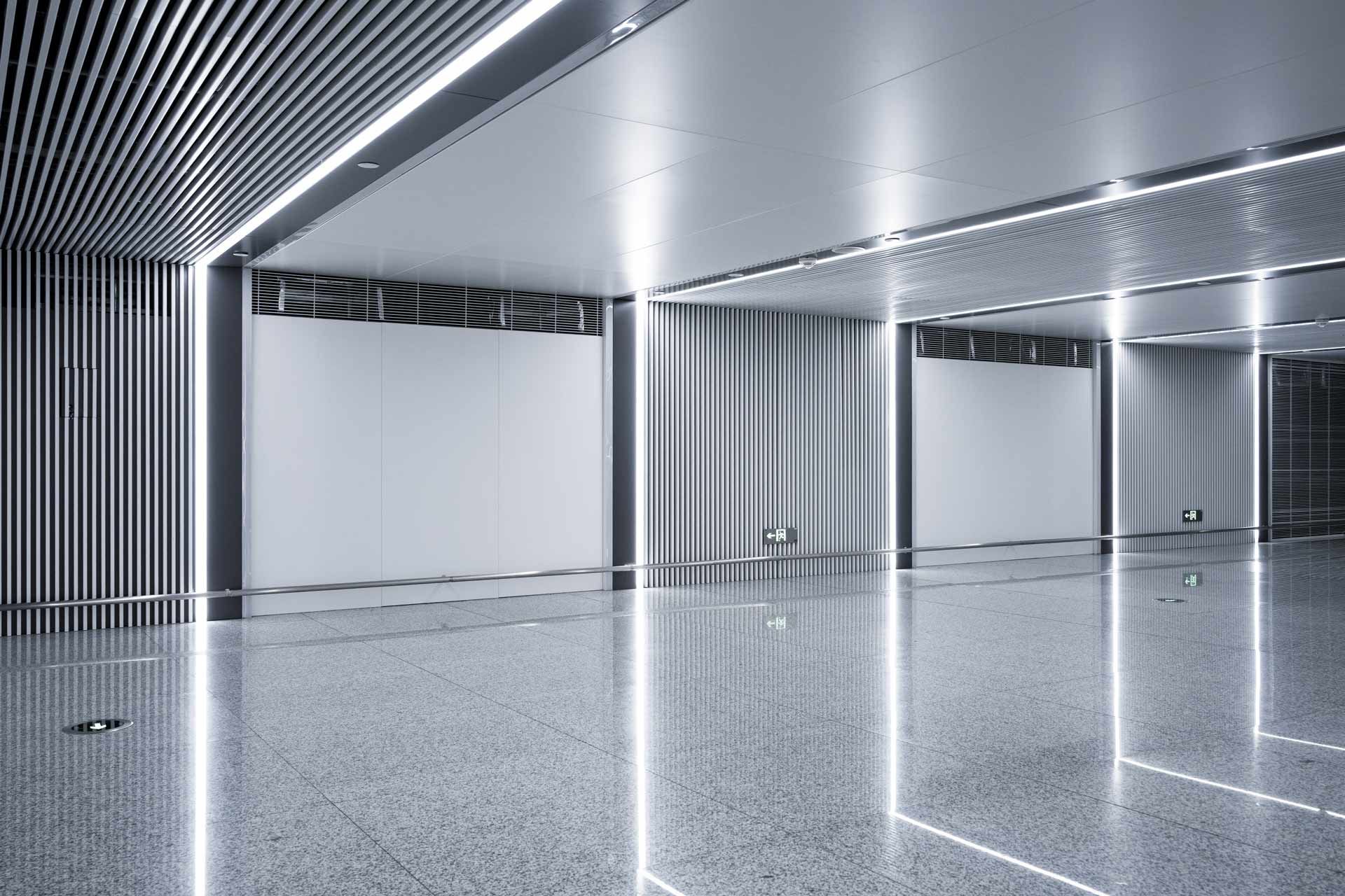 Modern, empty room with reflective floor and textured walls and ceiling. Bright overhead lights.