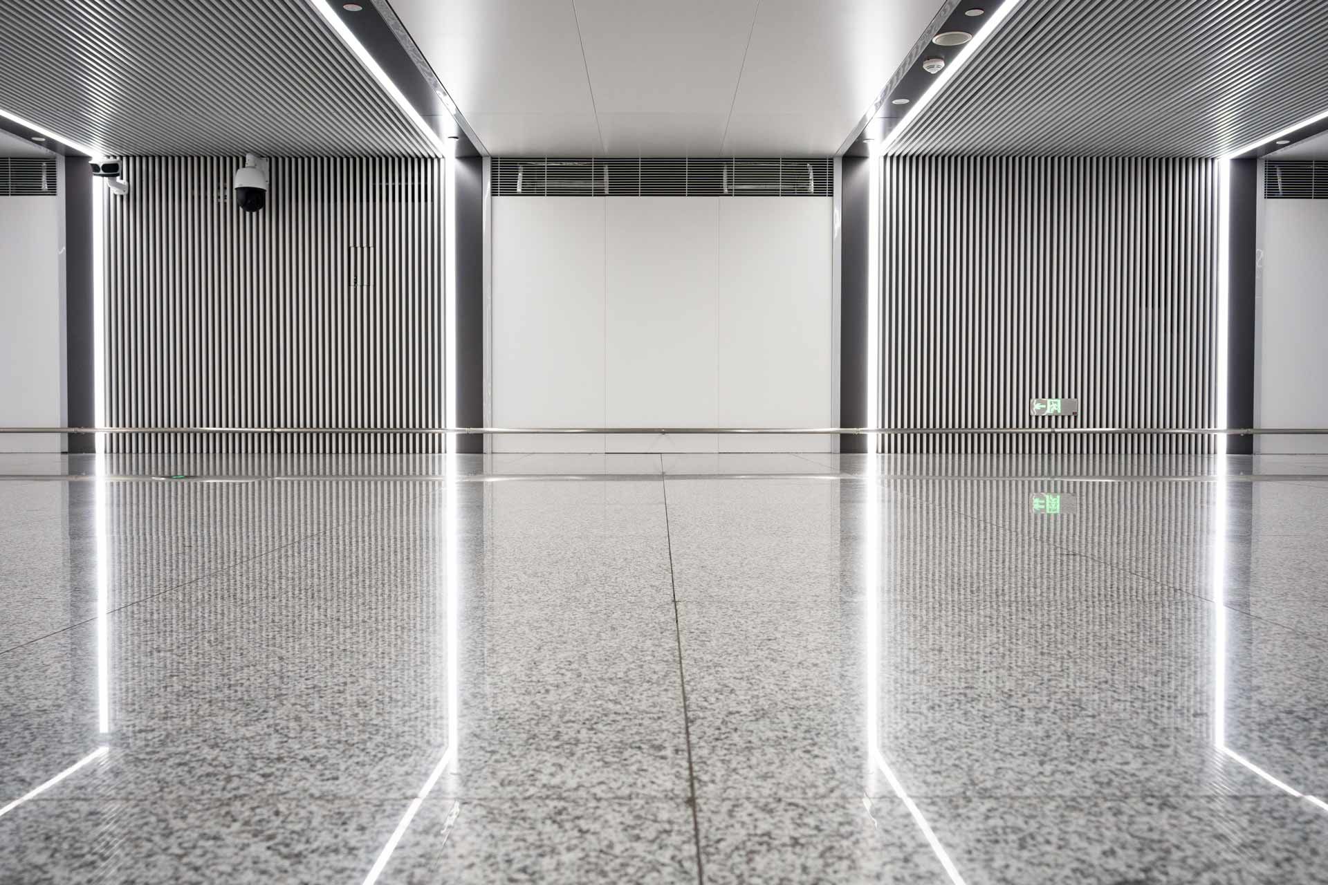 Reflective hallway with gray patterned walls, bright vertical lights, and a white end wall.