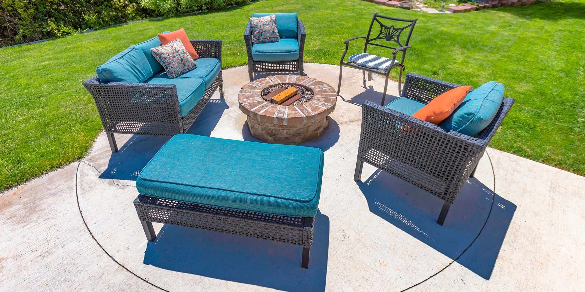 Patio furniture set with fire pit on a concrete patio, surrounded by green grass.