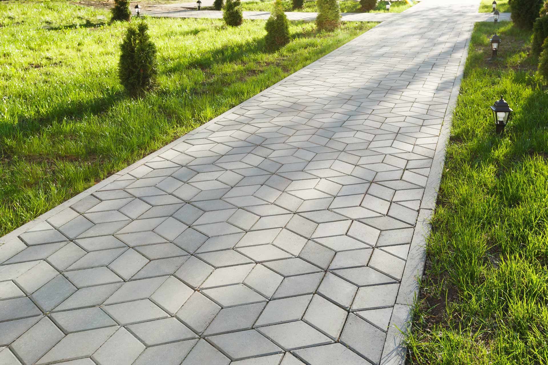 Gray geometric-patterned brick pathway through a grassy park.