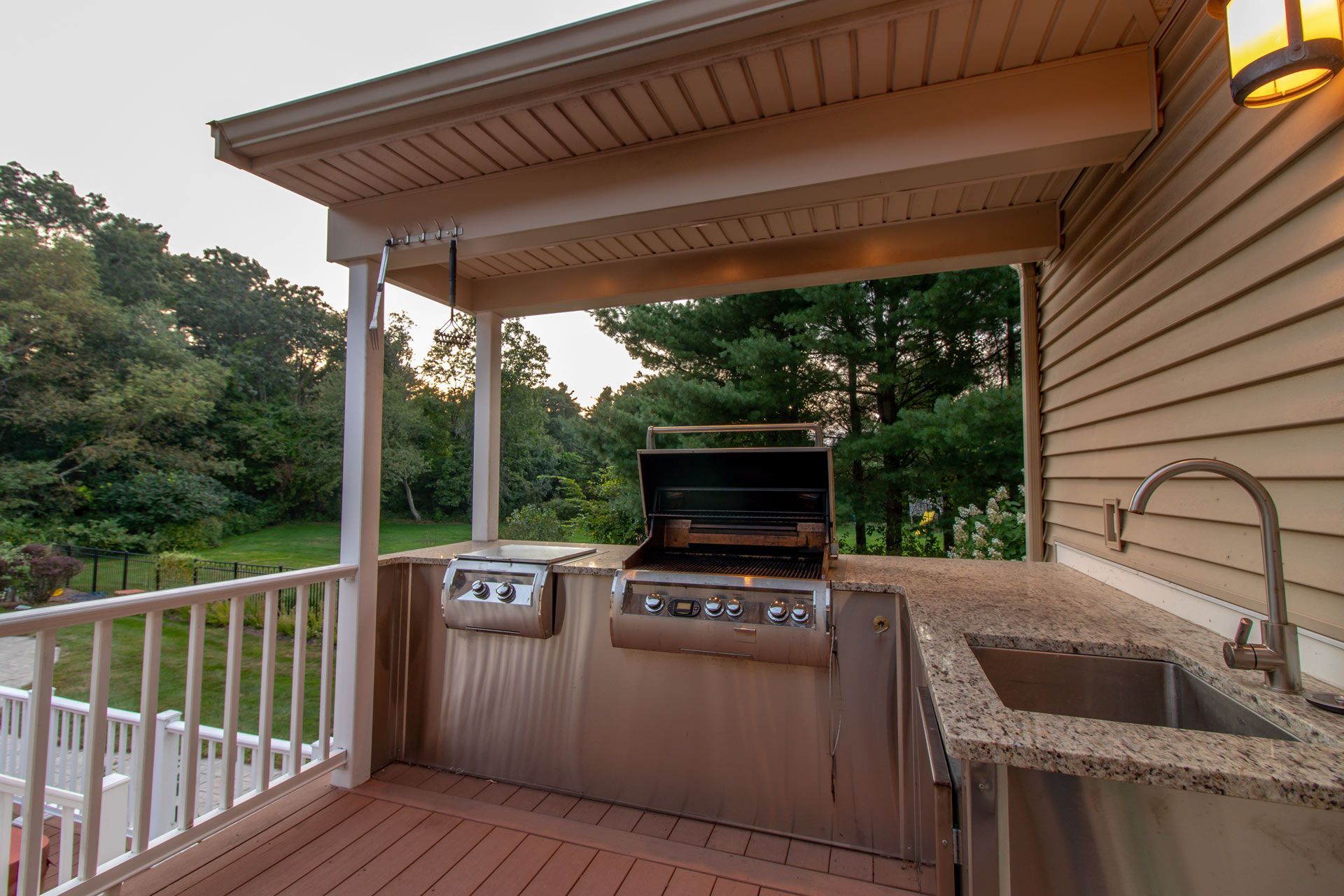 Outdoor kitchen on a deck with grill, sink, and surrounding trees.
