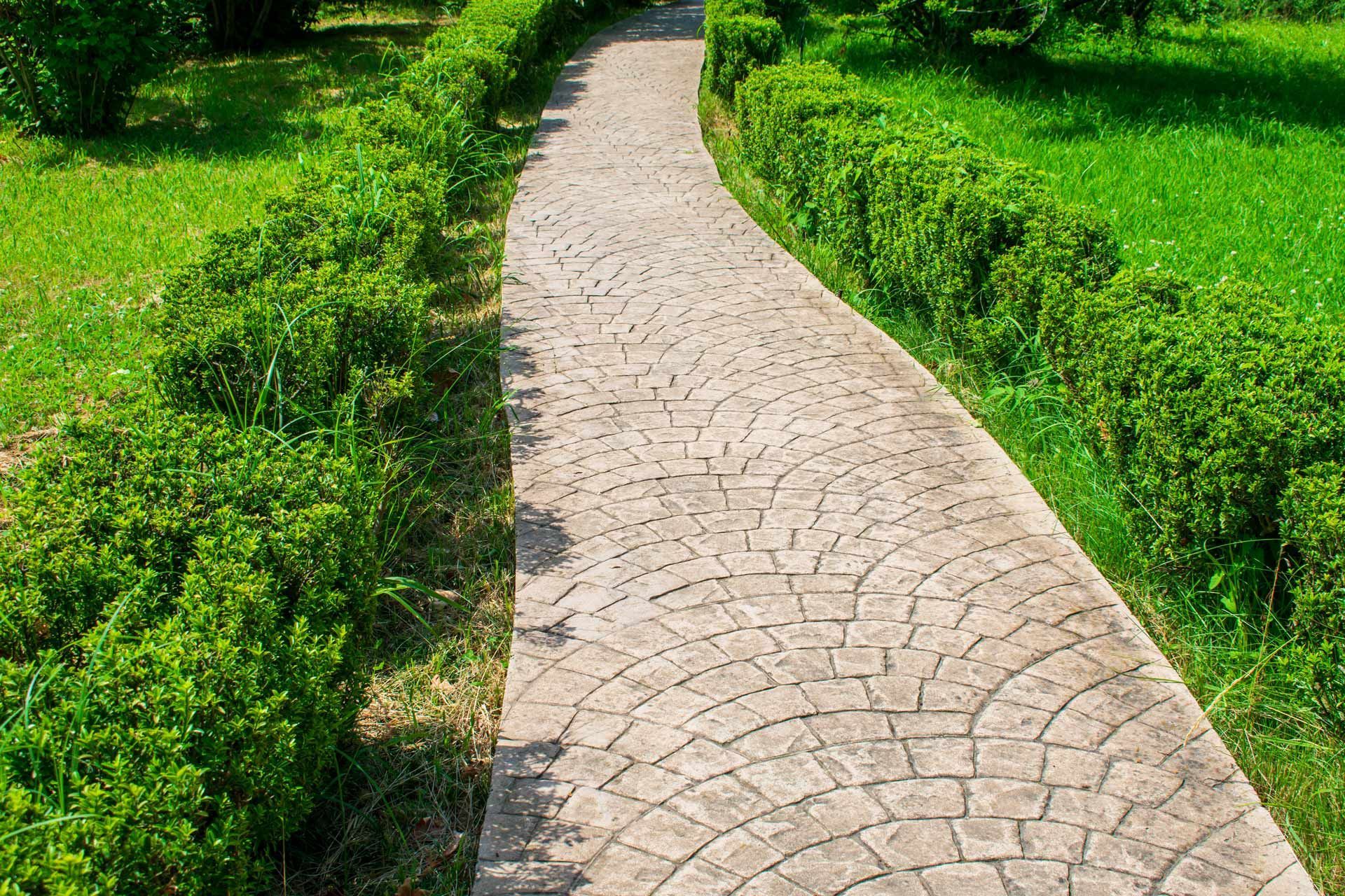 Stone pathway curves through a green garden, bordered by neatly trimmed bushes and grass.
