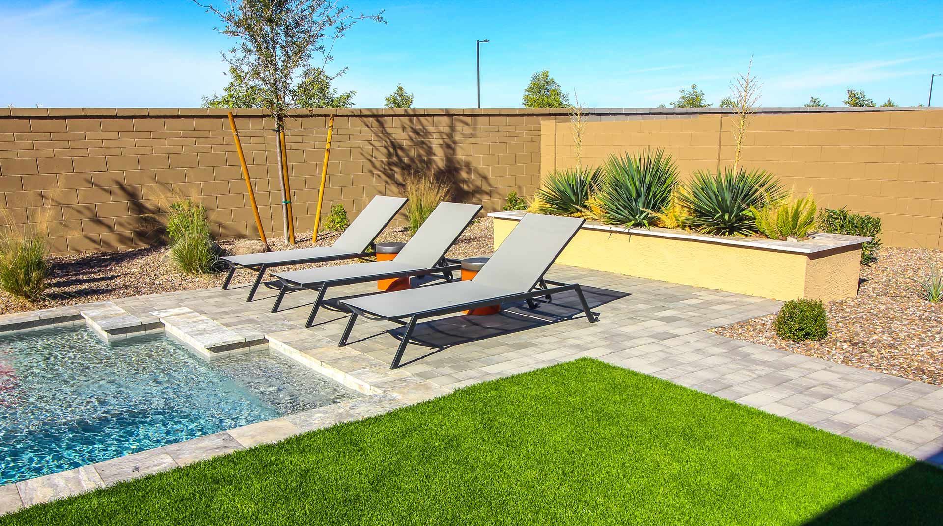 Lounge chairs by a pool in a backyard with a grass area and a raised planter bed.