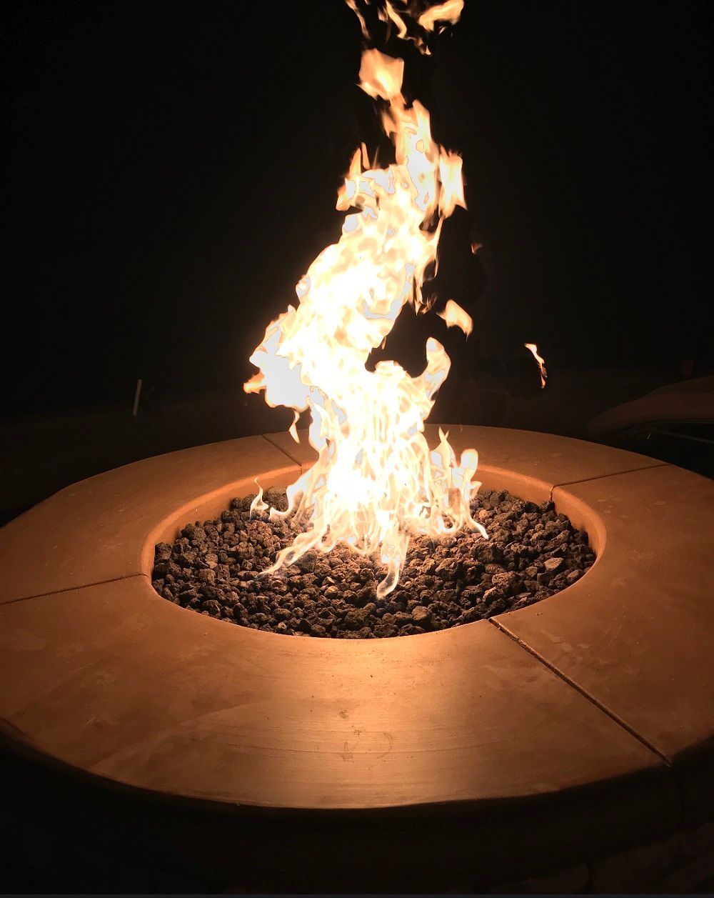 Fire burning in a circular fire pit with rocks; orange glow in a dark setting.