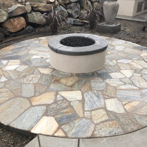Fire pit on a flagstone patio with rock background.