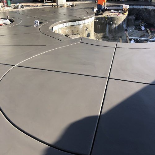 Newly poured gray concrete patio around a pool under construction.