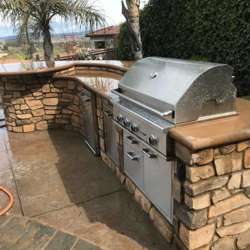 Outdoor stone grill station with stainless steel grill, cabinets, and countertop.