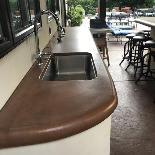 Outdoor kitchen countertop with a stainless steel sink, brown surface, and chrome faucet.