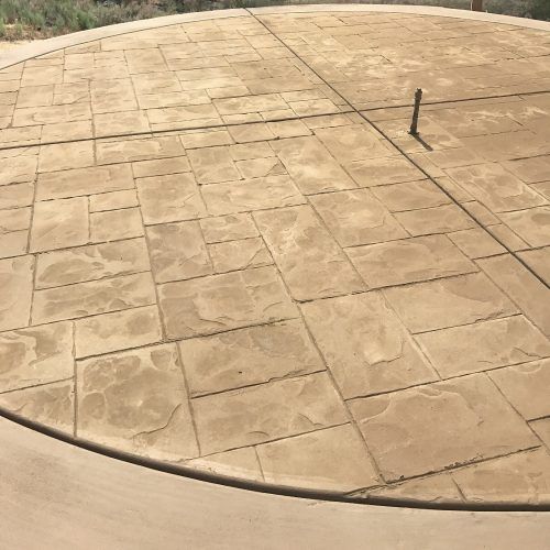 Circular, light brown, stamped concrete patio with a stone-like pattern, a concrete edge, and a small metal pipe.