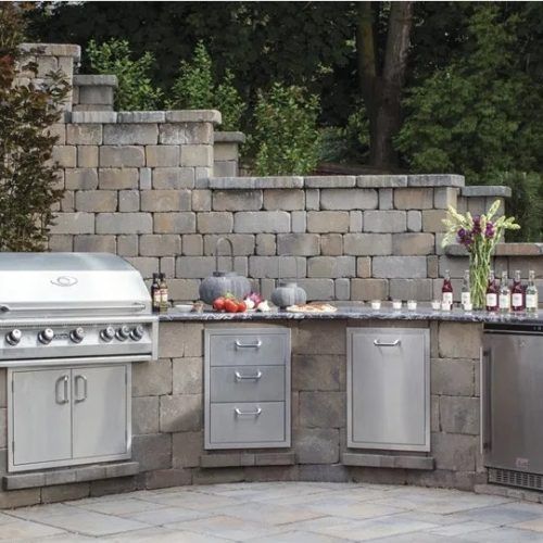 Outdoor kitchen with grill, drawers, fridge, stone walls, and counter.